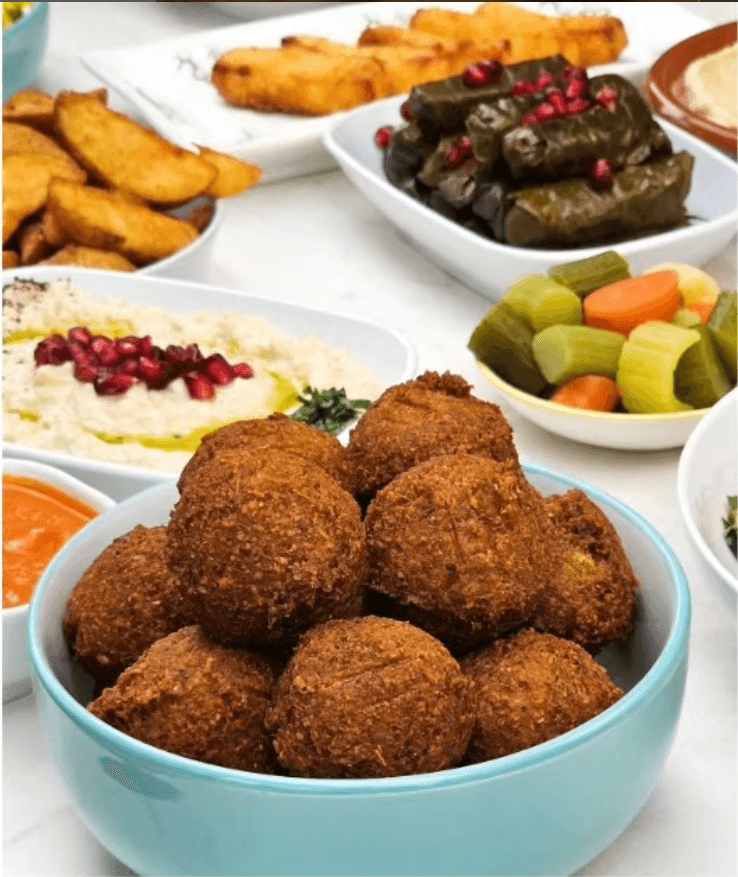 A bowl of falafel with hummus, pickles and wedges from a catering platter